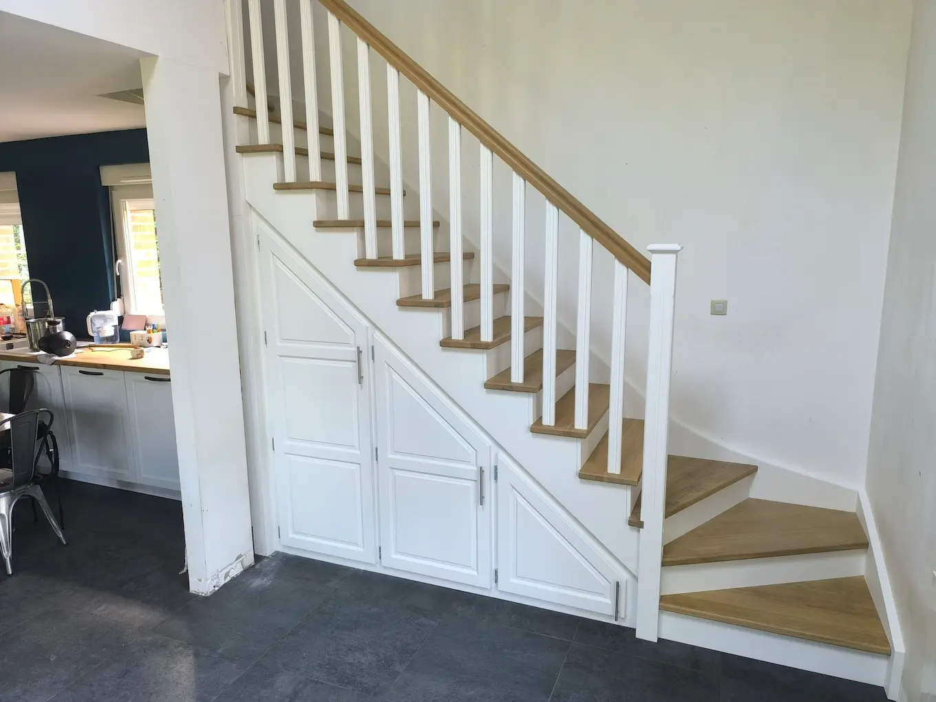 Aménagement de placards de rangement sur-mesure intégrés sous un escalier blanc.